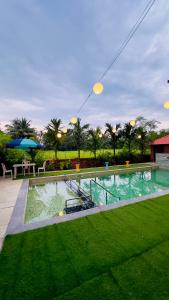 a swimming pool with green grass and an umbrella at Kashid Sunrise Resort in Kashid