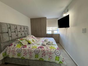 Acogedor Apartamento al oriente de Neiva في نيفا: غرفة نوم بسرير ولحاف ورد وتلفزيون +7 صور