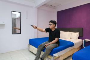 a man sitting on a bed holding a remote control at Griya Surya Hostel in Grogol