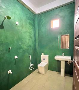 a green bathroom with a toilet and a sink at Maccan's Village in Arugam Bay