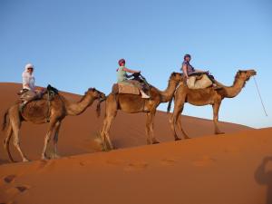 three people riding on the camel in the desert at Riad Aicha & Camel Trekking in Merzouga