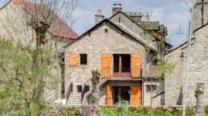 une vieille maison en pierre avec des portes orange et un balcon dans l'établissement Gîte Gîtes de France 2/4 personnes au Fau de Peyre, à Fau-de-Peyre