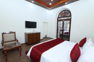 Un dormitorio con una cama, un televisor y una silla. en KSTDC Hotel Mayura Royal Heritage-Ooty, en Ooty