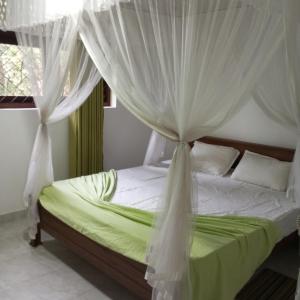 a bedroom with a bed with white curtains at Leafy Villa in Mirissa