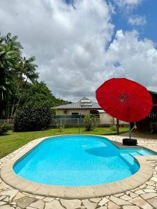 a red umbrella sitting next to a blue swimming pool at La Villa Louisia in Matoury