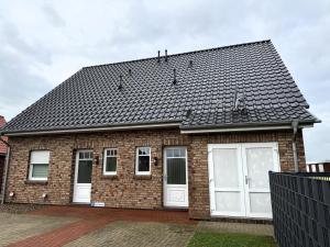 a brick house with white doors and a black roof at Ferienhaus mit Garten in Neßmersiel