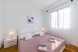a white bedroom with a pink bed with two towels at Apartments Luxury apartments in Ploče