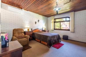 a bedroom with a bed and a chair and a window at Casa Tissot- 5 Quartos no Centro de Gramado in Gramado