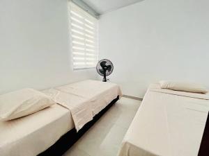 two beds in a white room with a fan at Alojamiento Aipe-Huila, cerca al Desierto-Tatacoa in Aipe