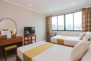 a hotel room with two beds and a desk and a window at Holiday Plaza Hotel - Cebu in Cebu City
