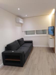 ein Wohnzimmer mit einem schwarzen Sofa und einem Flachbild-TV in der Unterkunft Beach House in Póvoa de Varzim