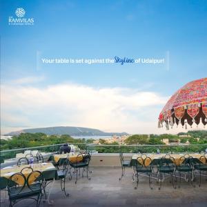 a balcony with tables and chairs and an umbrella at The Ramvilas - A Rooftop Pichola Lake View Hotel in Udaipur