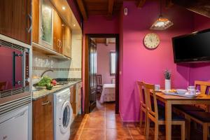 eine Küche mit lila Wänden, einem Tisch und einer Uhr in der Unterkunft Apto Rosa - Casa el gaitero in Susacasa