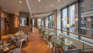 Un restaurante con mesas, sillas y ventanas. en Maldron Hotel Manchester Cathedral Quarter, en Mánchester