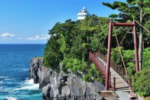 a suspension bridge with a lighthouse on a cliff at ジェムスティーイン川奈 in Ito