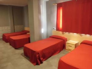 a room with three beds with red sheets and a window at Hostal Virginia in Favareta