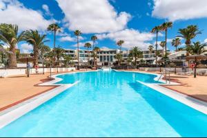 a large pool with palm trees and a hotel in the background at RockBeach bungalow in Costa Teguise