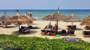 a group of people sitting on a beach with umbrellas at Hoi An Tháng 1 Villa in Hoi An