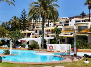 a swimming pool in front of a building with palm trees at Primera línea Aquamarina Anfi del Mar in Los Caideros