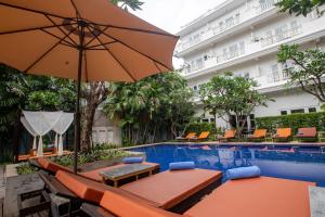 a hotel pool with tables and chairs and an umbrella at Amber Angkor Villa Hotel & Spa in Siem Reap