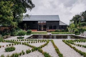 a garden with a pond in front of a black house at Silchester Farm in Mortimer West End