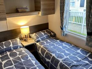 two beds in a room with a desk and a window at R&R Coastal Retreats Cedars 63 in Skegness