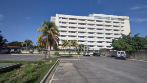 a large white building with a palm tree in front of it at Hermoso Apto Playero con Piscina in Cumaná