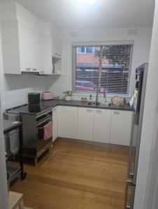 Una cocina con gabinetes blancos y un fregadero y una ventana. en Ground Floor Elwood village Apartment, en Melbourne