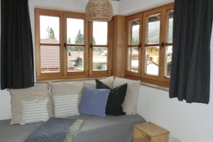 un salon avec un canapé avec des oreillers et des fenêtres dans l'établissement Bett & Berge - Ferienwohnung in den Schlierseer Bergen, à Schliersee