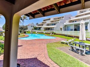 a patio with a table and a swimming pool at Beachfront Apartment Shakas Rock - Martinique, Pool, Ocean Views in Ballito