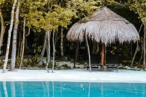 a straw umbrella and a bench next to a swimming pool at Villa Escondida - Riviera Maya in Puerto Morelos