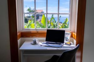 un computer portatile seduto su una scrivania di fronte a una finestra di Sleep Among the Bananas! Rustic Cottage with Trails at Your Doorstep a Ponta do Sol