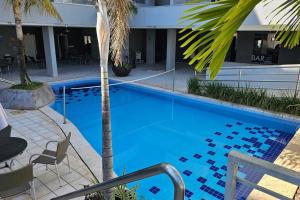 a blue swimming pool with a palm tree next to a building at Lindo Flat ao lado do Hot Park - Cond Serra Park -Apt 121 in Rio Quente