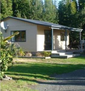 a small house with a porch in the yard at Ahipara Holiday Park in Ahipara