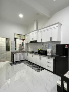 a kitchen with white cabinets and a black refrigerator at POKMA Homestay in Kampong Molek