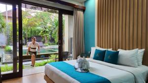 ein Schlafzimmer mit einem Bett und eine Frau, die nach draußen geht in der Unterkunft ABISHA Hotel Sanur in Sanur