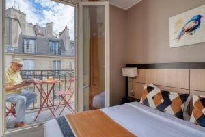 un homme assis à une table à l'extérieur d'une fenêtre dans une chambre dans l'établissement Hotel Phenix Paris, à Paris