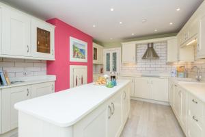a kitchen with white cabinets and a pink wall at Beach Front House with Stunning Sea Views and Free Use of a Local Indoor Pool in Talland