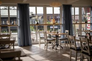 a dining room with a table and chairs and windows at Kallehavegaard Badehotel og Restaurant in Løkken