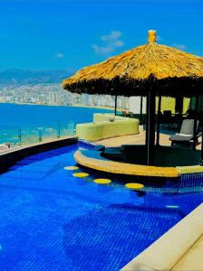 una piscina con sombrilla de paja y el océano en 3 Atardeceres, Pet Friendly Vista al Mar en Brisas, en Acapulco