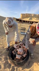 two men cooking food on a grill on the beach at Qusoor elarab Camp in Qaryat Ḩātim aţ Ţāʼī