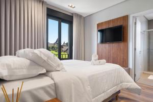 a white bedroom with a large bed and a television at Requinte a passos da Rua Torta by Achei Gramado in Gramado