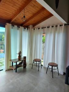 a room with white curtains and a table and two stools at Chalé Vista pra Lombada in Conceição da Ibitipoca