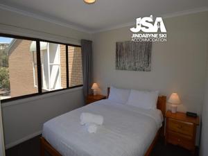 Un dormitorio con una cama con sábanas blancas y una ventana. en Alpine Mountain View 40, en Jindabyne