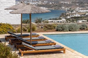 a row of lounge chairs and an umbrella next to a swimming pool at Acron Villas Paros in Kolympithres