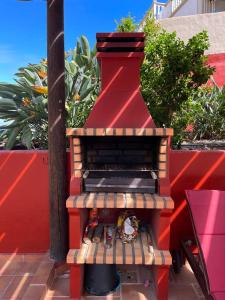 Una parrilla al aire libre con una pared roja y plantas. en Casa Rural La Pitanga, en Hermigua