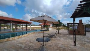 a patio with a table and an umbrella next to a pool at Casa Portal das Flecheiras in Trairi