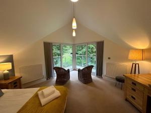 a bedroom with a bed and chairs and windows at Trewhiddle Retreat V17 by Together Travel - Luxury 4-Bedroom Villa in St Austell