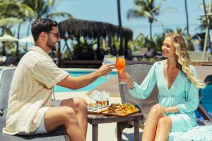 a man and woman sitting at a table with drinks at Ritz Lagoa da Anta Hotel & SPA in Maceió