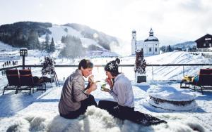 two people sitting in the snow eating food at Mirador Apartments in Seefeld in Tirol